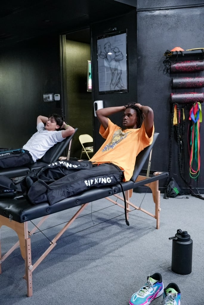 Two athletes relaxing on treatment tables wearing pneumatic compression recovery boots at Pulse Check in Dallas