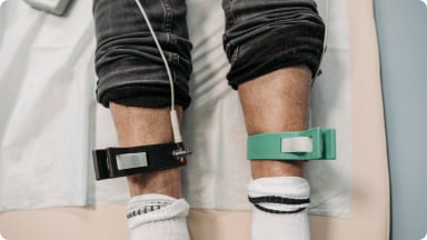 Patient seated on a treatment table with straps placed on both lower legs during a physical therapy session