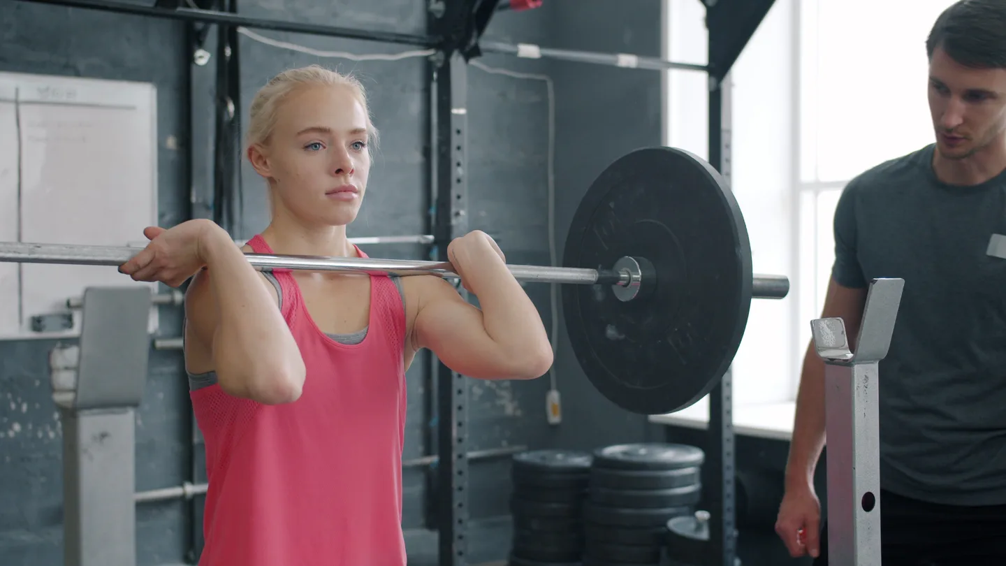 Young athlete lifting weights with a coach guiding her form